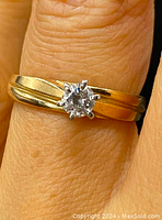 Close-up front view of ring on finger showing round diamond solitaire in six-prong setting on yellow gold band