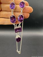 Photo showing full length of chunky sterling silver necklace with multiple deep purple amethyst stones in ovular, rectangular, and teardrop shapes.