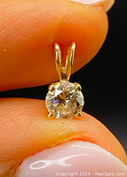 Front view of pendant held between fingertips showing round diamond face and gold prong setting