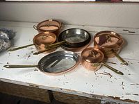 Overview of six copper and brass cookware pieces arranged on white surface