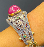 Close‐up of top of cuff showing large oval cabochon ruby, triangular diamond slices, emerald and sapphire accents, micro pave diamonds