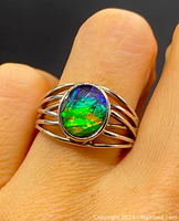 Close-up photo of the Ammolite ring on finger showing vibrant green, blue, purple colors in oval stone set in sterling silver split band.