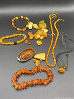 Full view of assorted amber jewelry laid out on black background including necklaces, bracelets, loose stones, and a metal framed amber piece.