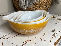 Side view of four nested vintage glass mixing bowls with yellow and white floral patterns.
