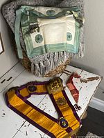 Group shot of apron, purple and gold sash, and red collar displayed on table