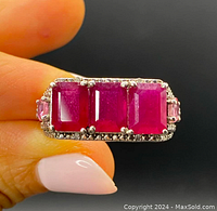 Close-up front view of ring showing three large rectangular cut natural rubies centered with smaller pink sapphires on each side, and diamond accents around the border.