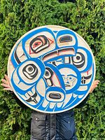 Front view of the round wood plaque leaning against greenery showing full formline design and color palette