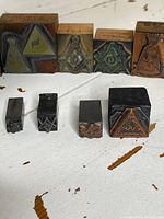 Front view of five wooden block stamps in back row and four loose metal dies in front, all displaying Masonic symbols