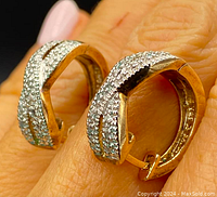 Close-up side profile of earrings on fingertips showing two-tone finish and pavé diamonds.