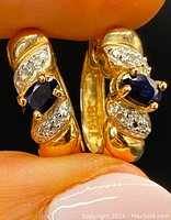 Close-up front view of one earring showing central oval sapphire flanked by diamond clusters