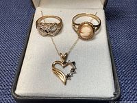 Three jewelry pieces displayed in presentation box: heart pendant necklace and two rings