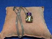 Chain and pendant displayed on brown cushion against blue background