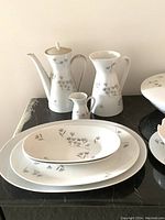 Image of coffee pot with lid, pitcher, creamer, and assorted plates including oval and round shapes with floral pattern.