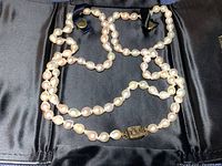 Full view of necklace with two strands of irregular shaped pearls and metal clasp on black fabric background.