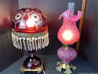 Two cranberry glass lamps side by side on a black background, both illuminated
