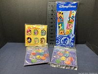 All four sets of Disney pins arranged against a ruler for size reference, showing packaging and pin designs