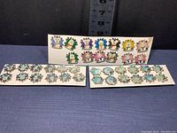 Three white cards with Disney snowflake shaped trading pins arranged in rows showing colorful character faces and snowflake bases.