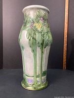 Front view of tall cylindrical ceramic vase with green drip glaze and leaf motif.