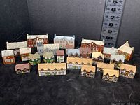 View of entire set of 24 Wade vintage miniature ceramic buildings arranged in rows with a height scale visible at the back showing all buildings less than 2 inches tall.