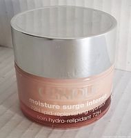 Photo of front of pink jar with silver lid showing Clinique Moisture Surge Intense branding and key product name.