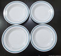 Four white round diner plates with turquoise and black concentric rings around the edge, arranged in a square pattern.