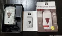 Electric shaver in original packaging with instruction manual and charging cable.