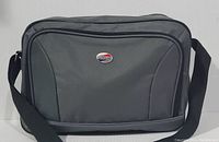 Front view of the gray American Tourister travel bag showing general shape, front pocket, and shoulder strap.