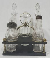 Frontal view of the four glass condiment/cruet bottles placed in the black wooden stand with brass accents