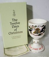 Photo of the goblet standing next to the original box and certificate showing the front design with two turtle doves, red lettering on the base, and partial box text.