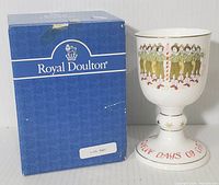 White bone china goblet decorated with ten drummers around a striped pole, gold accent trim and red 'TWELVE DAYS OF CHRISTMAS' script on base, approximately 6 inches tall.