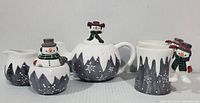 Front view of ceramic snowman tea set showing all five pieces with winter icicle and snowflake design, and snowman figures.