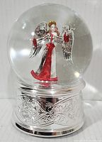 Front view of the musical snow globe showing angel figurine in red and silver inside clear globe with silver ornate base.
