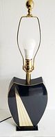 Front view of the 1980s Italian table lamp showing black lacquer base with brass design, brass neck, and light bulb socket with harp.