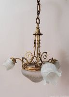 Full view of three-arm chandelier with metal frame and frosted glass shades shaped like flowers.