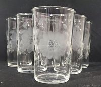 Front view of five clear vintage juice glasses with etched frosted cornflower floral design visible on each glass.