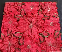 Close-up photo showing detailed red poinsettia embroidery with bead accents and cutouts on table accent fabric.