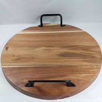 Show front top view of round wooden board with metal handles