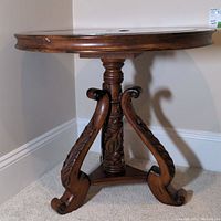 Side view of the round accent table showing heavily carved wooden pedestal and scrolling supports beneath stone top.