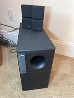 Front and side view showing one Bose Acoustimass 5 series subwoofer speaker and two satellite speakers placed on top