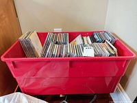 Red plastic storage bin filled with several rows of CDs stacked upright and lying flat.