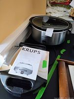 Photo showing the Crock-Pot slow cooker with glass lid and Krups waffle maker with its instruction manual on the side.