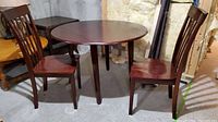 Photo of wooden dining table with drop leaf top and two matching chairs, showing condition and style.