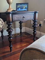 Front and side angled view showing the dark wood side table with a single drawer, turned legs, and metal ring pull handle.