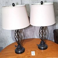 Pair of matching metal spiral twist cage style table lamps with white fabric shades on a wooden table.