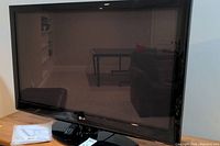 Front view of the LG 42 inch plasma television showing the screen and base stand, along with the remote and manual placed nearby.