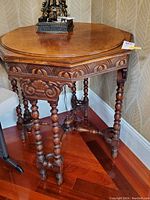 Front left angle view of the Mersman octagonal wooden accent table showing carved apron and turned legs.