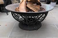 Side view showing metal bowl style fire pit with ornamental scrollwork and wood inside the bowl.