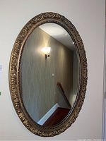 Full view of the oval mirror hanging on the wall reflecting light and wallpaper.