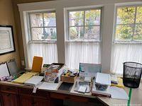 Wide view of office supplies on windowsills including paper stacks, notepads, boxes, and containers.