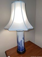 Full view of the pottery lamp lit, showing the floral design on the base and white fabric shade.